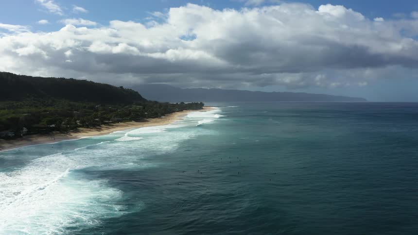 Aerial view of the horizon with a beach down below where people are swimming in the water at daytime
