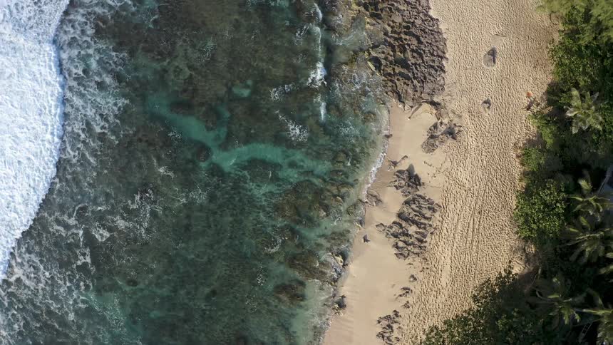 Twisting top down aerial view of ocean waves crashing over the rocks in the coast