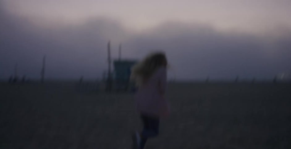 A man chases and grabs at a woman as she attempts to evade him on a beach on a cloudy evening
