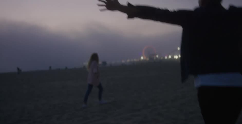 A man and woman lift their arms up to the sky as they run on the beach