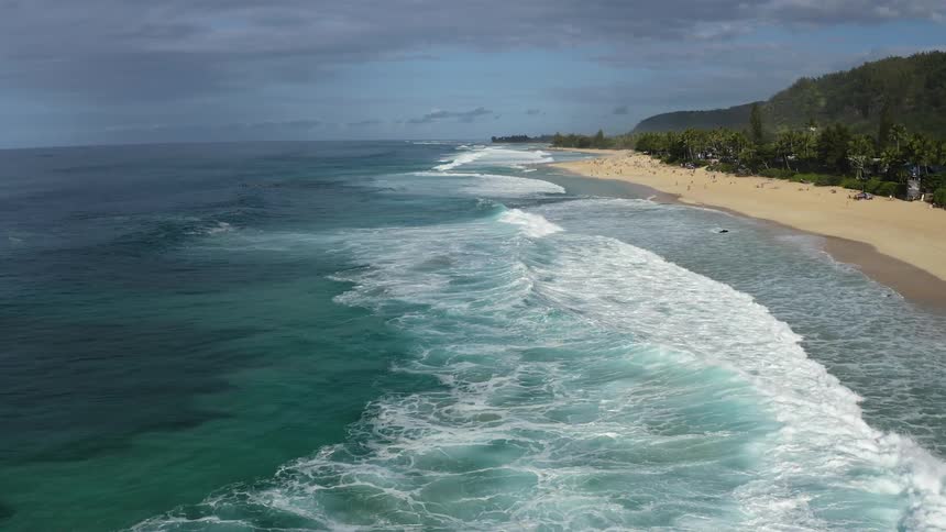 Aerial view of waves rolling in to a beach with people on it