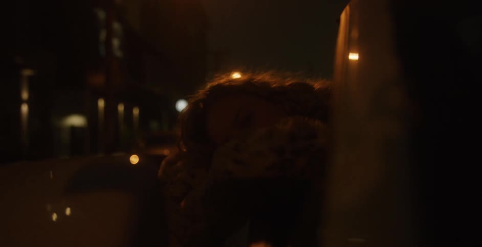 A woman with her head out a window of a moving car lying down at night