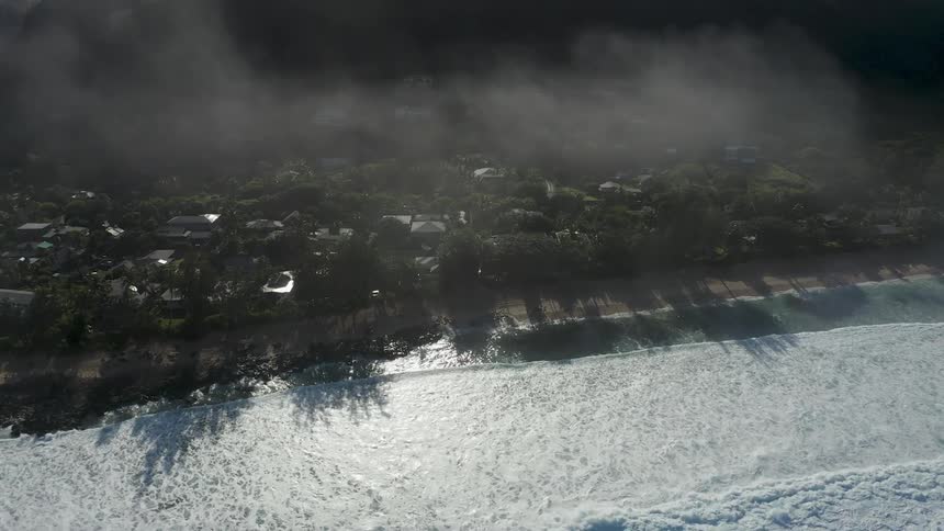 Aerial view of the tide coming in from the ocean towards beach houses and a neighborhood as fog comes down from above at daytime