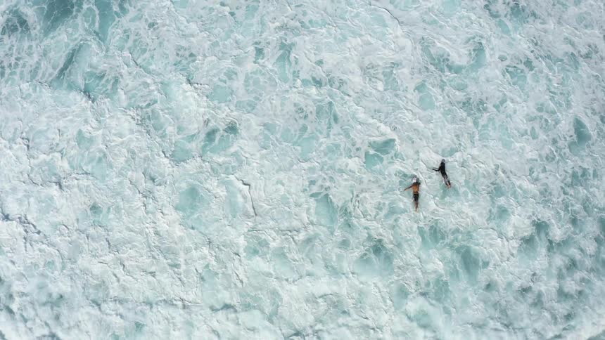 Two surfers paddle in the ocean and are overcome with a large wave