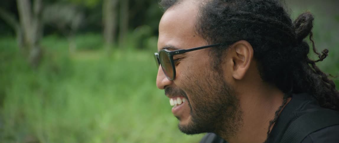 A man with glasses and gloves smiling with trees and grass in the background