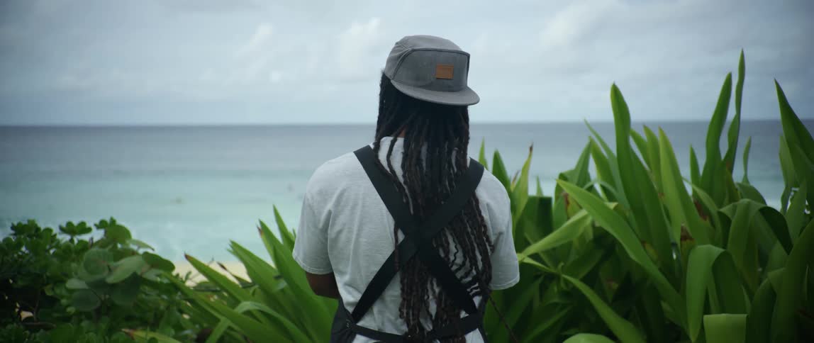 Black man standing next to some plants looking over to the sea