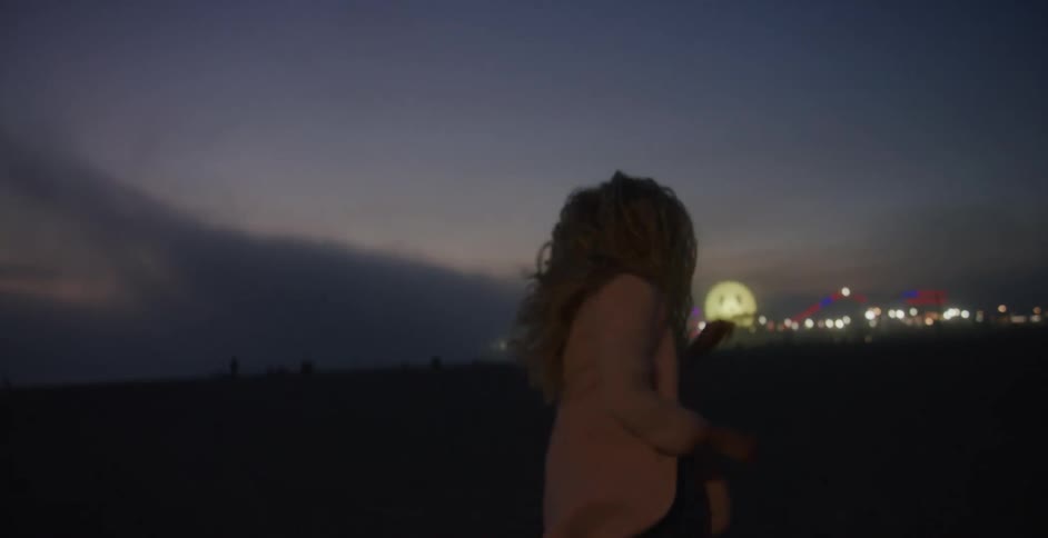 A woman peaks back at the camera as she runs along a beach on the coast of a city at night