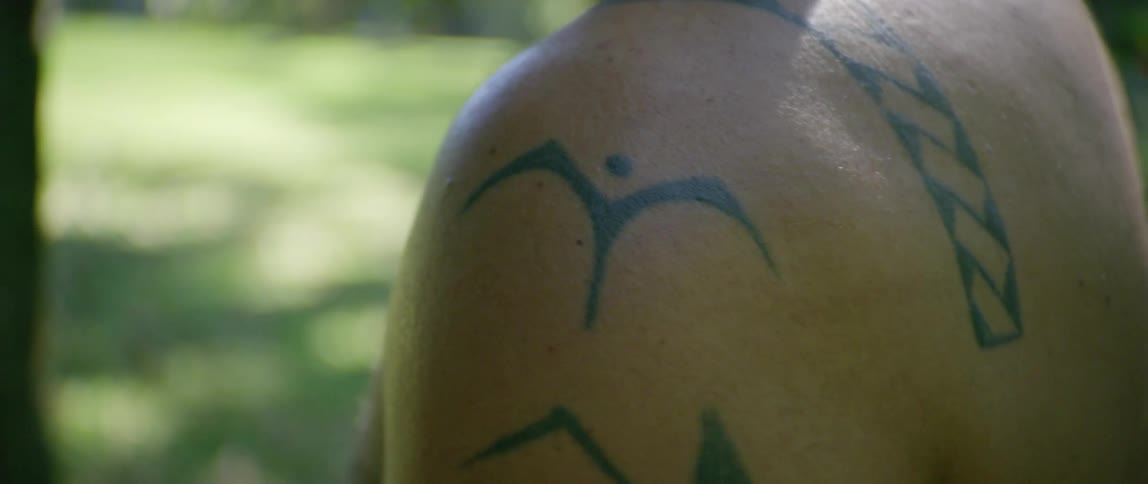 Back tattoos on a shirtless man standing outside at daytime