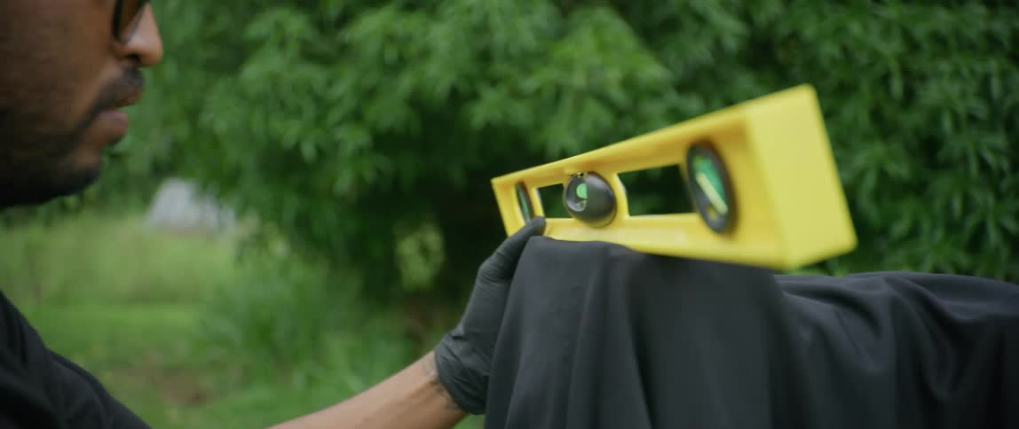 A man with dreadlocks and glasses looks at a yellow level outdoors
