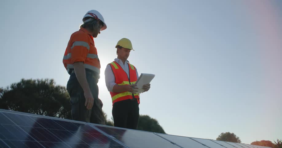 Construction workers check blueprints next to solar panels at evening