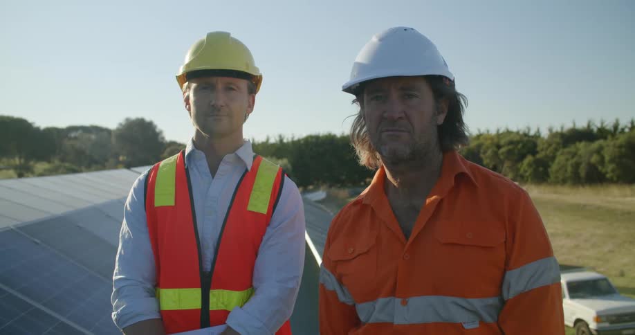 Two construction workers wearing hardhats standing on the roof of a building at evening