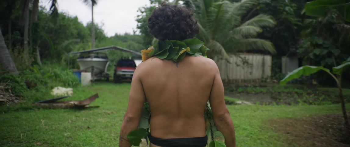 Man wearing hawaiian native attire walking to a house in a rural area of the island