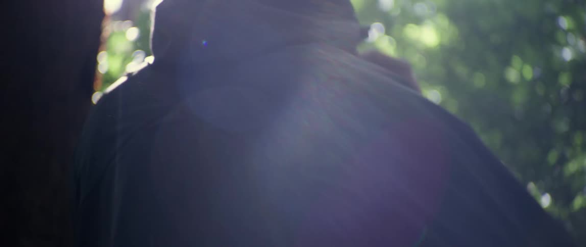Back of a man arranging the hood of a jacket while walking on the forest