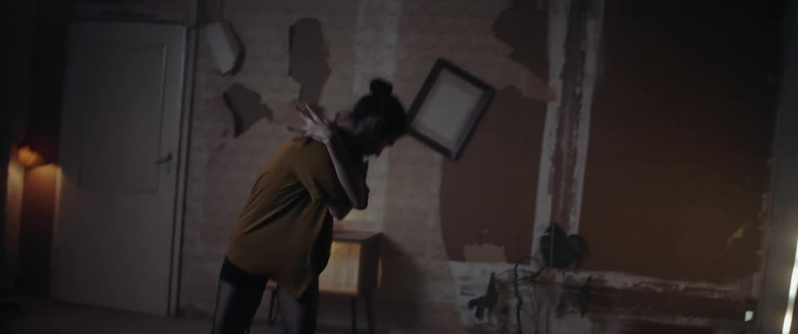 Woman dances in room with peeling wallpaper and damaged walls