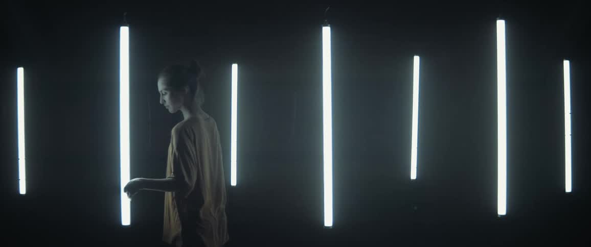 Young woman touches floating fluorescent lights inside a dark room