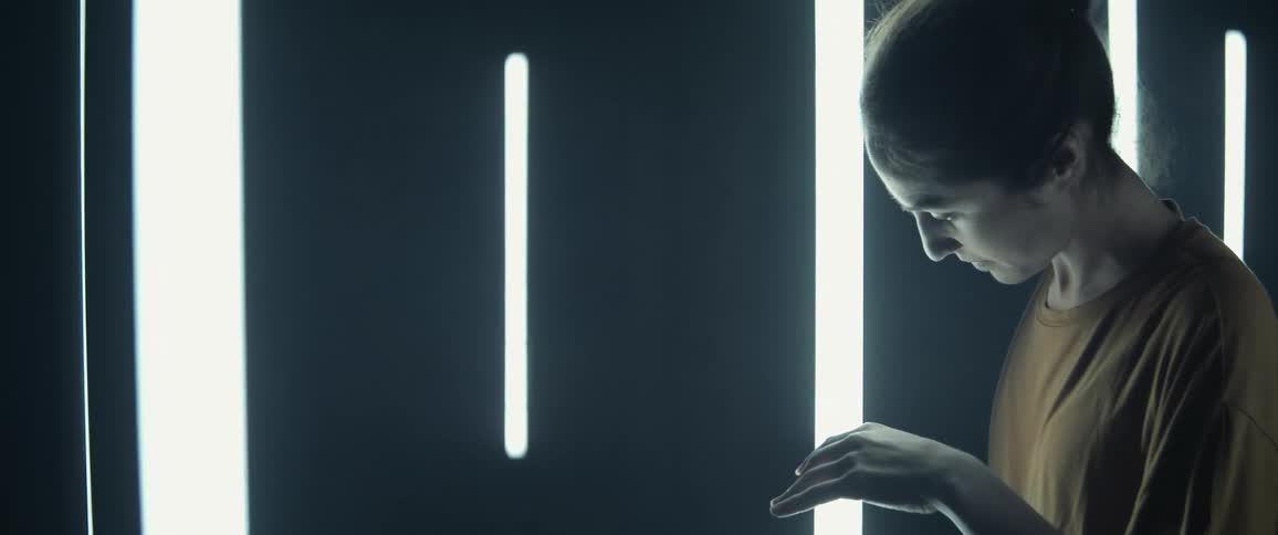 A woman in a room with lights glowing on the walls performs a dance move lifting her hand into the air