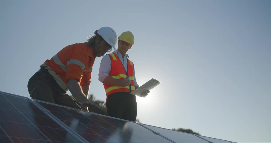 A man runs his hand over the surface of a solar panel while talking to his boss on a rooftop on a sunny day