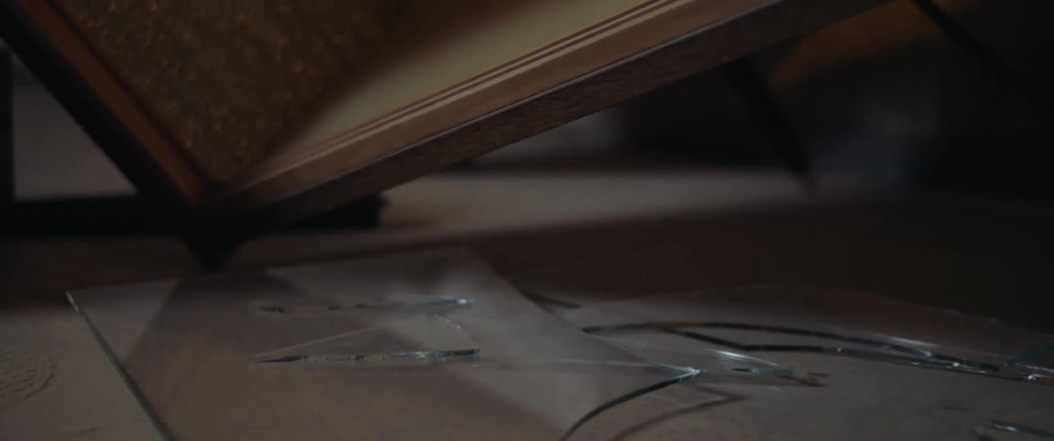 Shards and pieces of broken glass on the floor next to upturned furniture in a room