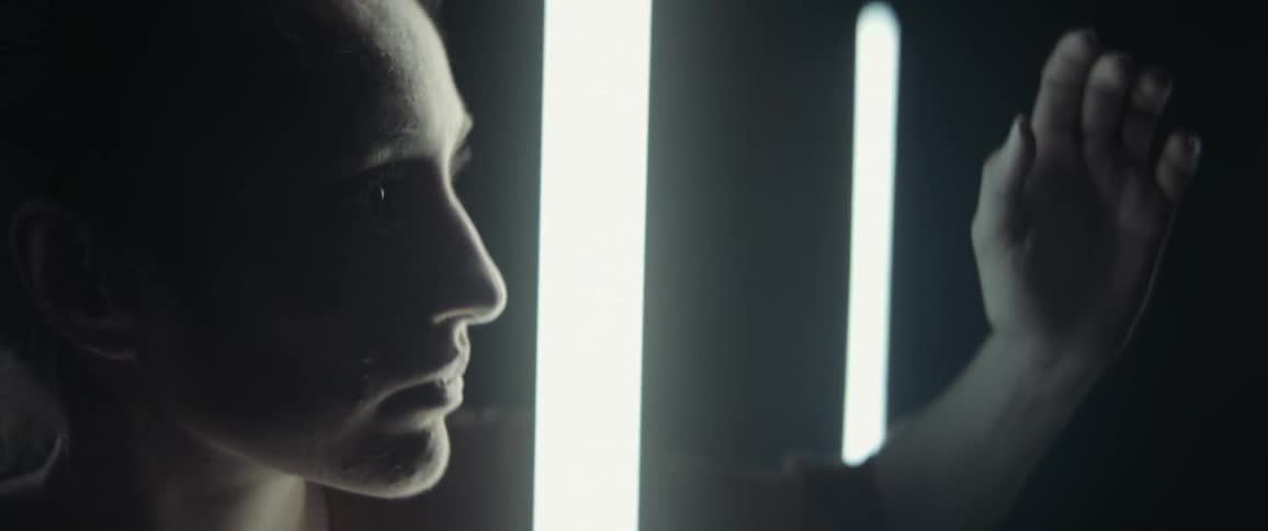 A woman puts her hand between two thin light fixtures and stares at it curiously