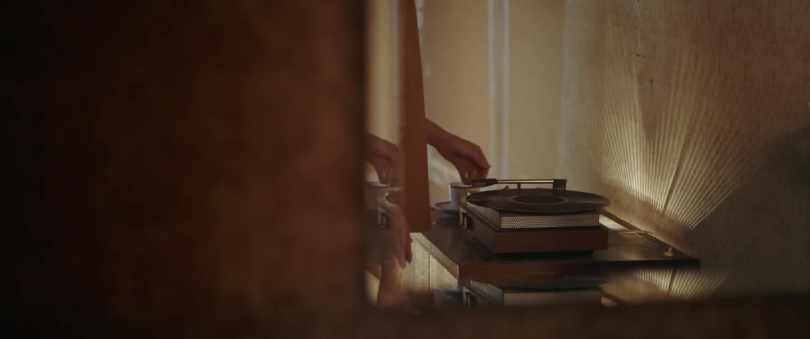 A mirror hanging on a wall reflects a person placing a vinyl record on a record player