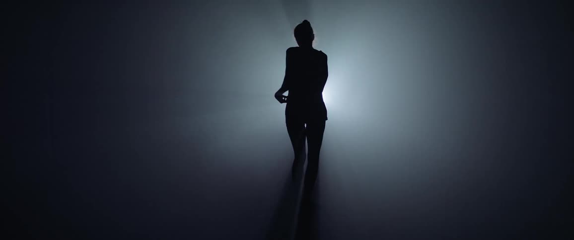 A woman is silhouetted dancing in front of a light that flashes white and purple