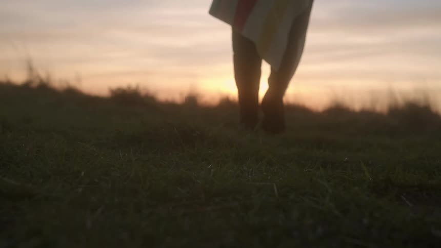 A person wrapped in blanket walking outside on grass at sunset