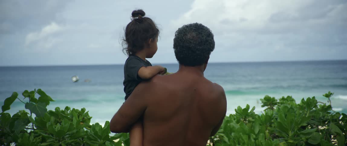 Father holding daughter on his arms looking at the ocean in a tropical beach
