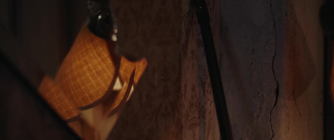 A lamp with a fabric shade flickers on and off in a dark room with concrete walls