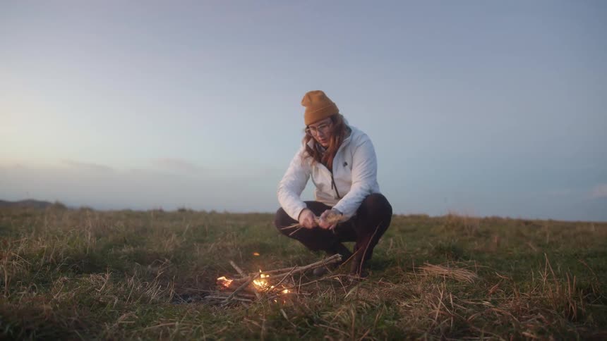 White woman starting a bonfire alone in a grass field