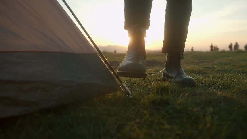 A man pushes a tent peg in to the ground with his boot