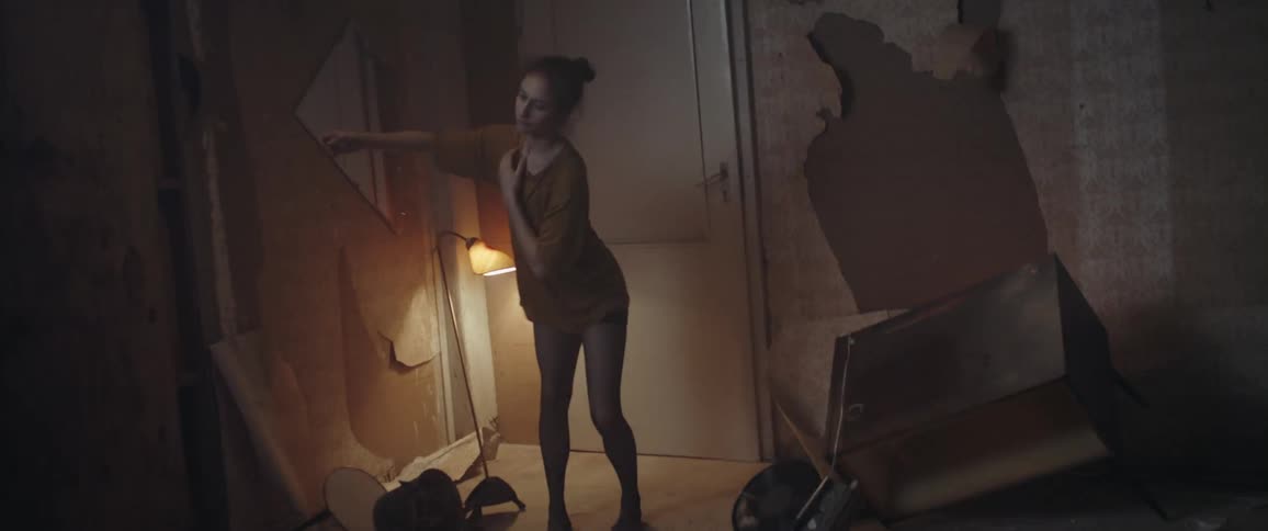 A woman doing contemporary dance in a trashy looking room in front of a strobe lamp