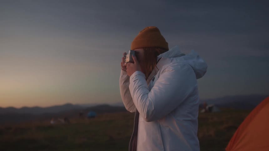 A female taking photographs outside in a field near a tent