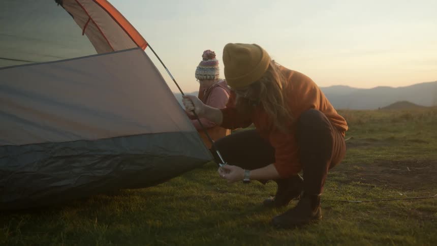 A woman and older child attempt to put a tent up outside in a rural setting