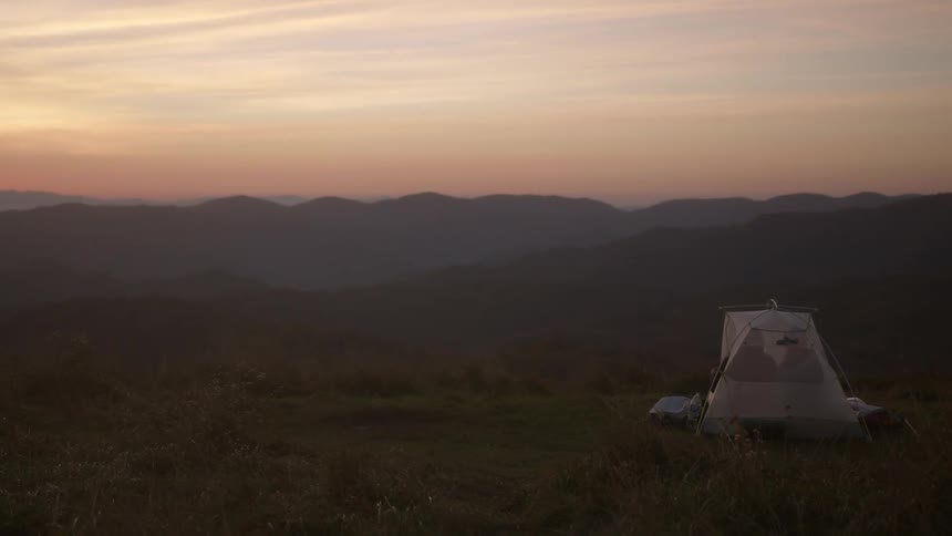 Couple camping on a small translucent tent in the mountains at sunset