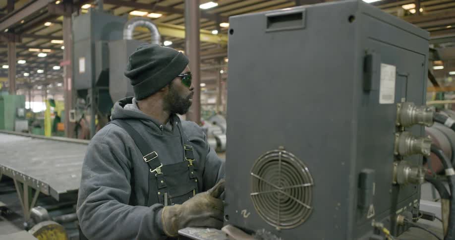 A factory employee works on a machine and hits a switch to make the backside emit a purple light