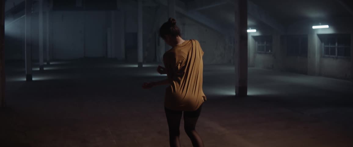 Woman performs dance moves inside of a large empty building