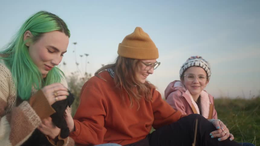 Group of white girls petting a dog and talking while sitting in the grass