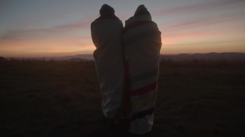 Two people walking at dusk wrapped in blankets