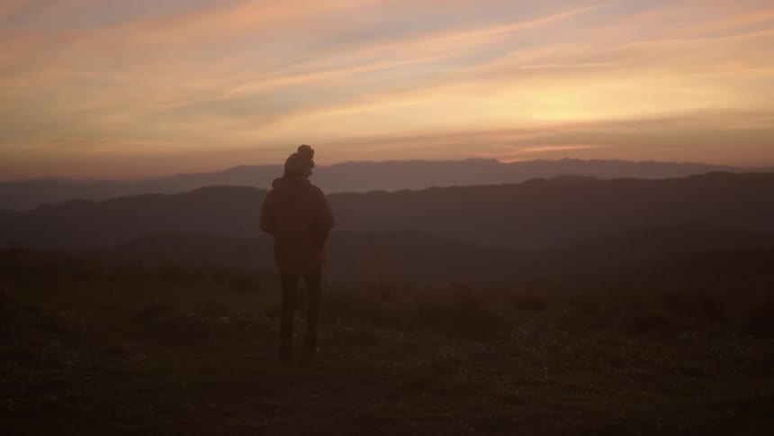 Woman walks towards the mountains at dusk