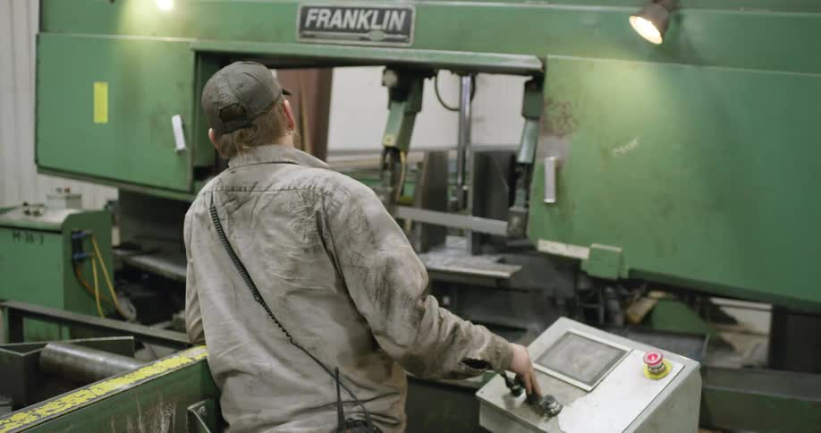 Man operating a large green machine at a small station in a warehouse building