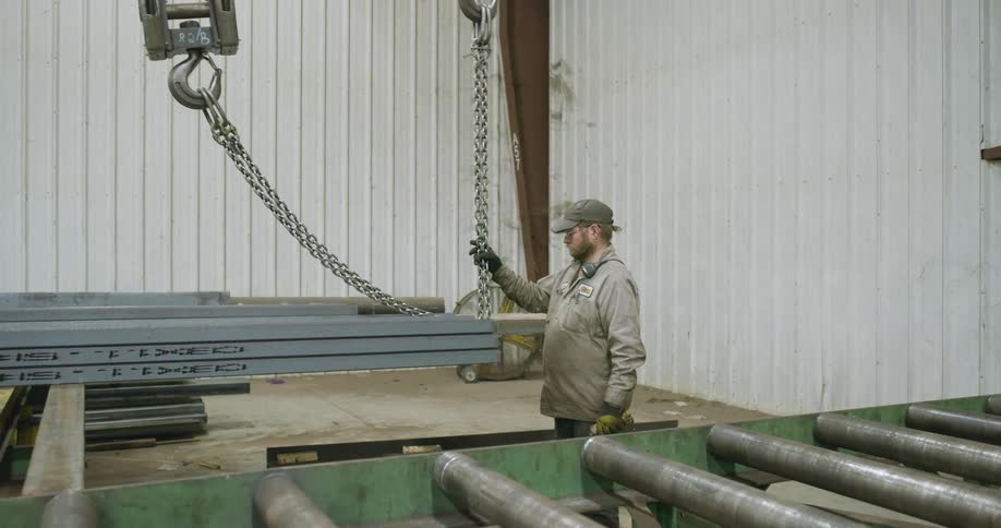 A man in a workshop attaches chains to steel being lifted up