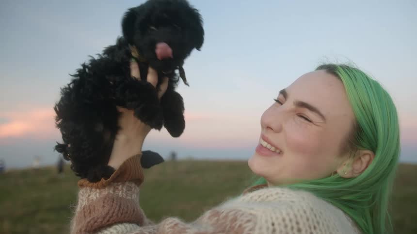 Teenager girl holding a puppy on her hands and laughing when it licks her nose