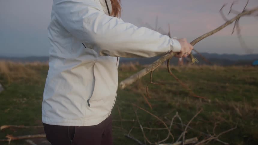 A teenage girl out camping breaks up a tree branch
