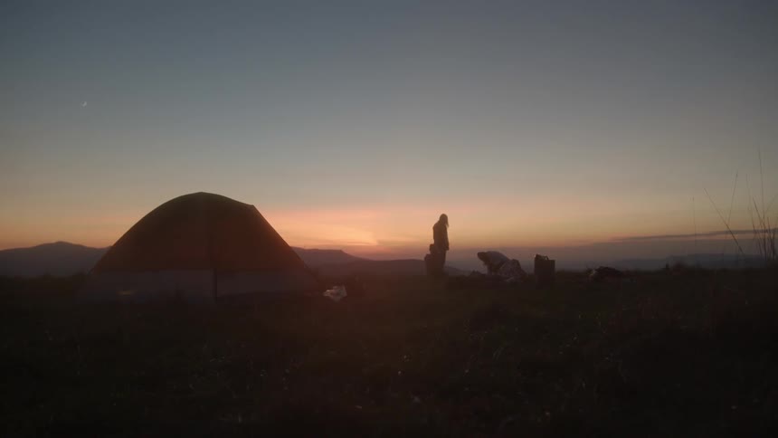 People camping outside their tent as the sun sets