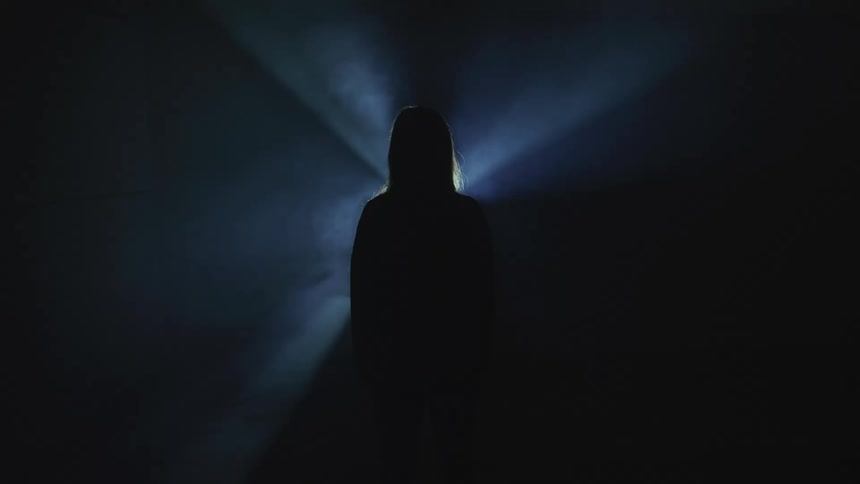 A silhouette of a person standing with a light flashing in the background