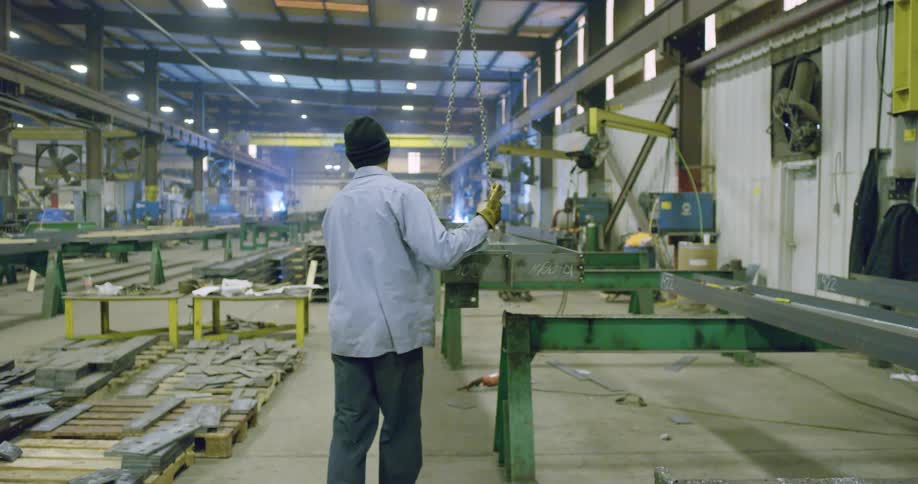 Metal worker pushing a metal frame on a crane inside a factory