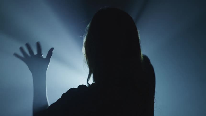 Woman dancing alone moving her arms in front of a flashing light in a dark room
