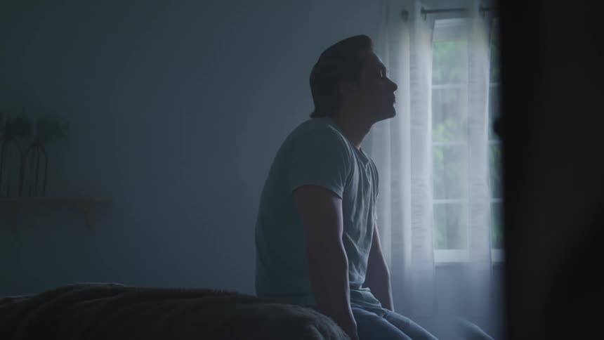 A man sitting on the end of his bed looking up in thought