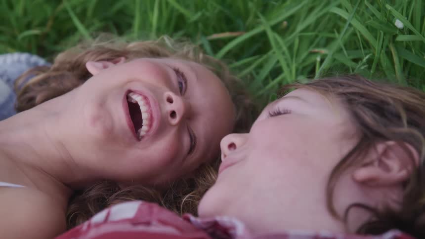 Two girls are laying in the grass laughing with one another