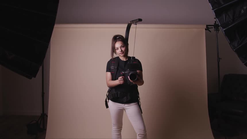 Woman holding photography equipment stands in front of a photo shoot set up and looks up at a camera